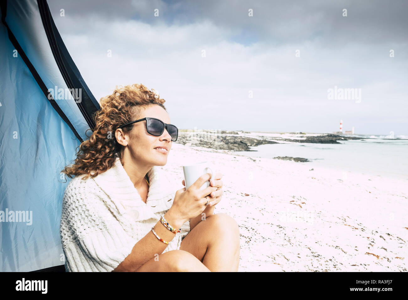 Bella la mezza età donna sedersi al di fuori di una tenda in spiaggia gratis camping outdoor sentimento della natura mentre bere un tè o un caffè da un bianco Cup - Vittoria Foto Stock