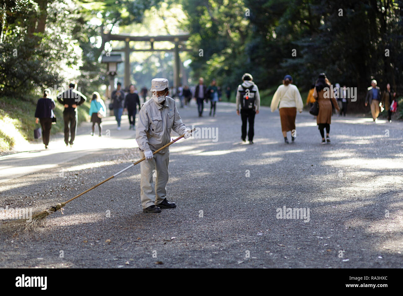 Il Tempio di Meiji, Yoyogi Park Harayuku, Tokyo Giappone - un tempio lavoratore è spazzare il terreno a torii gate lungo le boscose approccio al Tempio di Meiji Foto Stock