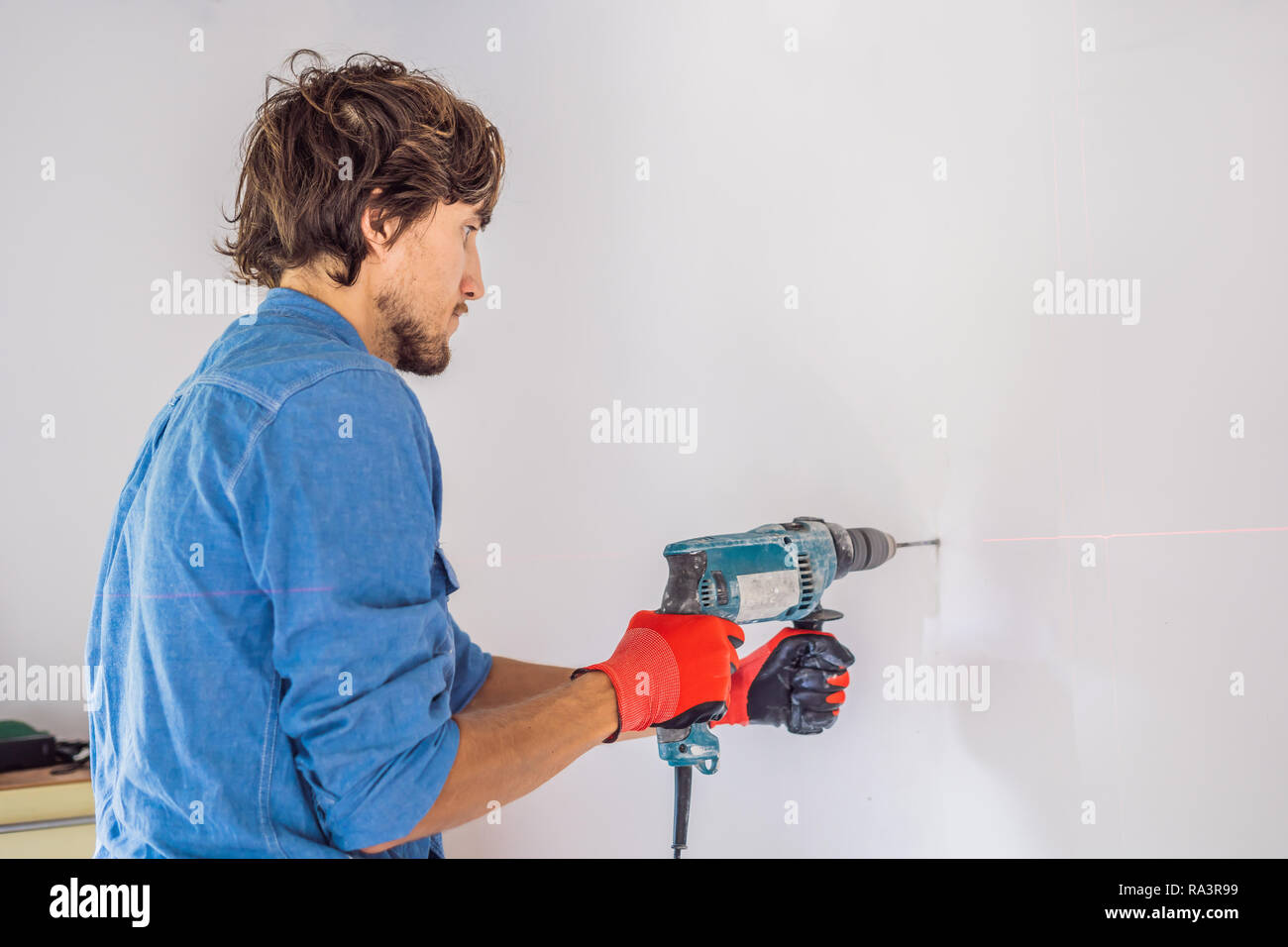 Un uomo che fa un buco nel muro con un trapano Foto stock - Alamy
