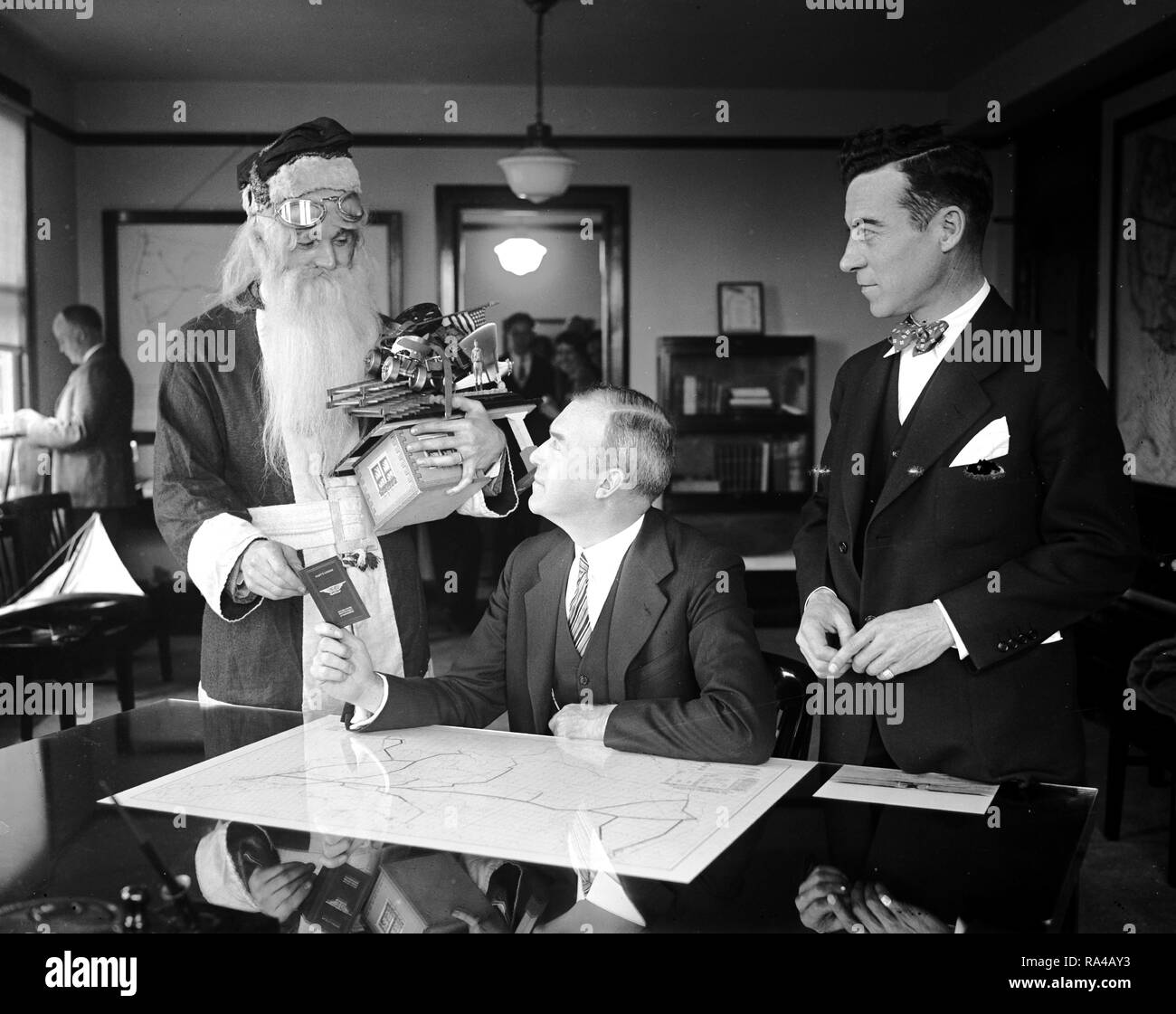 Babbo Natale riceve aereo licenza di pilota dal Segretario Assistente di commercio. Sebbene non vi può essere sufficiente la neve per la sua renna slitta, Babbo Natale sarà ancora in grado di consegnare il suo carico di presenta in tempo questo Natale utilizzando il percorso dell'aria. La vecchia San chiamati al ministero del commercio a Washington oggi dove egli è illustrato nella ricezione di un aereo licenza di pilota dal Segretario Assistente di commercio. per l'Aeronautica William P. MacCracken, mentre Clarence M. giovani (a destra) Direttore dell aeronautica, il Dipartimento del Commercio, guarda a. Foto Stock
