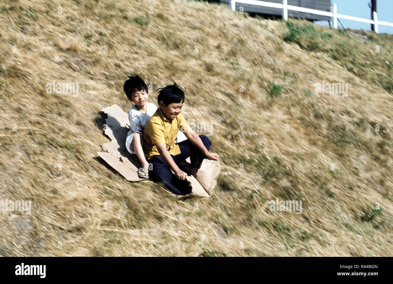 1975 - Bambini scorrere su una collina a una temporanea struttura alloggiativa per rifugiati vietnamiti. Foto Stock