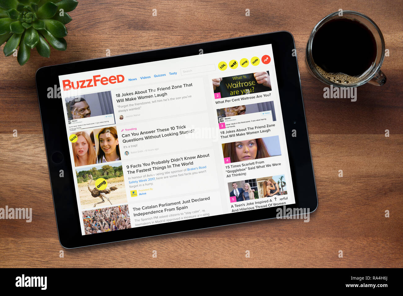 Il sito web di BuzzFeed è visto su un tablet iPad, su di un tavolo di legno lungo con un caffè espresso e una pianta di casa (solo uso editoriale). Foto Stock