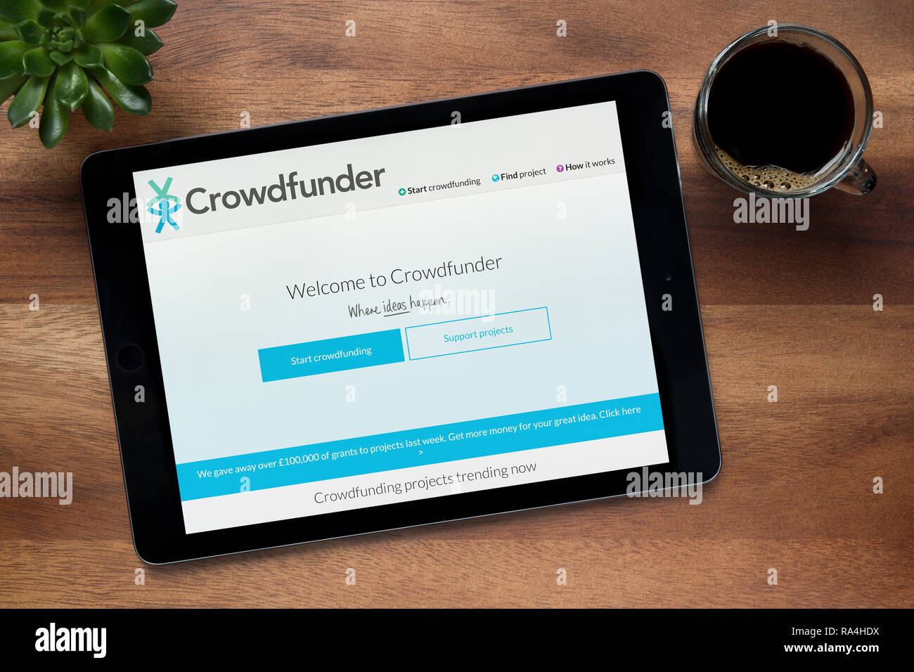 Il sito web di Crowdfunder è visto su un tablet iPad, su di un tavolo di legno lungo con un caffè espresso e una pianta di casa (solo uso editoriale). Foto Stock