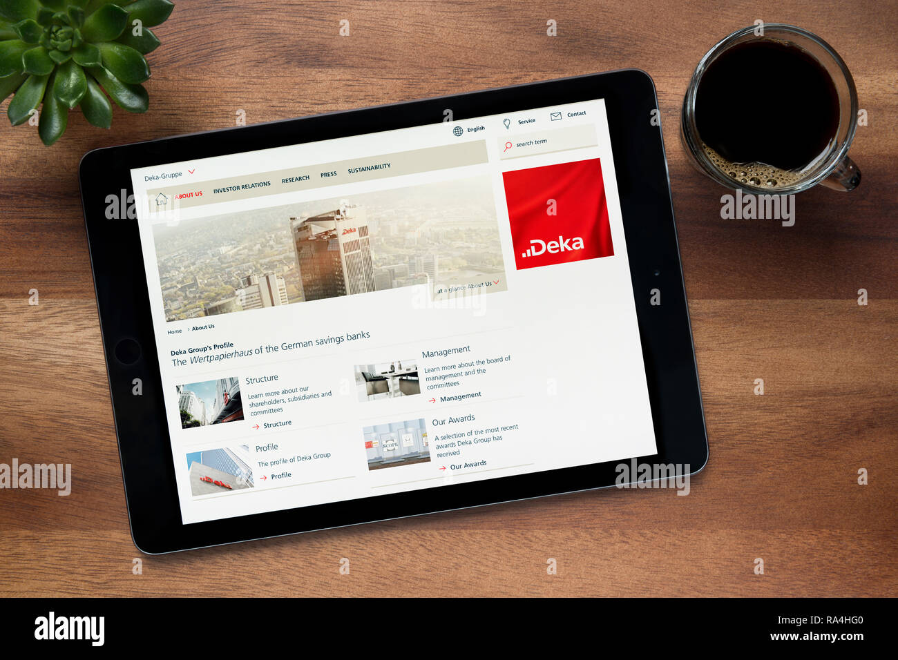 Il sito web di DekaBank è visto su un tablet iPad, su di un tavolo di legno lungo con un caffè espresso e una pianta di casa (solo uso editoriale). Foto Stock