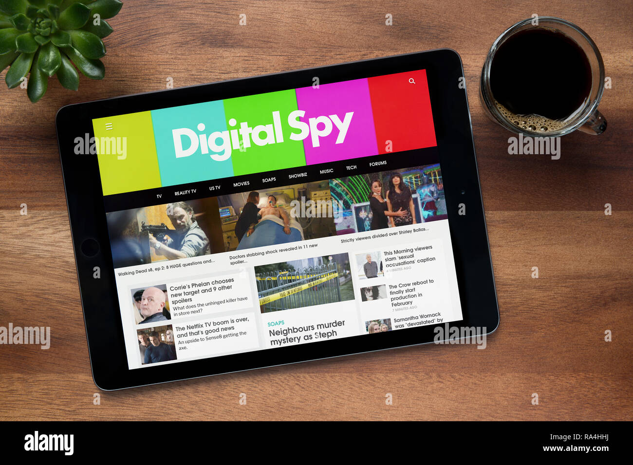 Il sito web di Digital Spy è visto su un tablet iPad, su di un tavolo di legno lungo con un caffè espresso e una pianta di casa (solo uso editoriale). Foto Stock