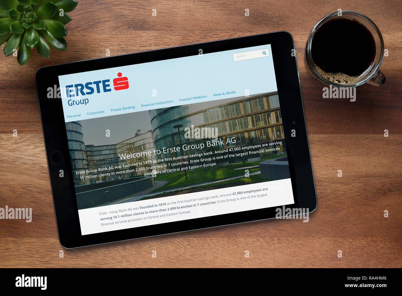 Il sito web di Erste Group è visto su un tablet iPad, su di un tavolo di legno lungo con un caffè espresso e una pianta di casa (solo uso editoriale). Foto Stock