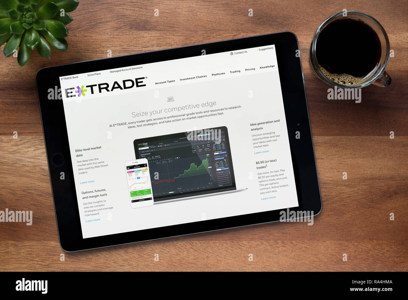 Il sito web di E*TRADE è visto su un tablet iPad, su di un tavolo di legno lungo con un caffè espresso e una pianta di casa (solo uso editoriale). Foto Stock