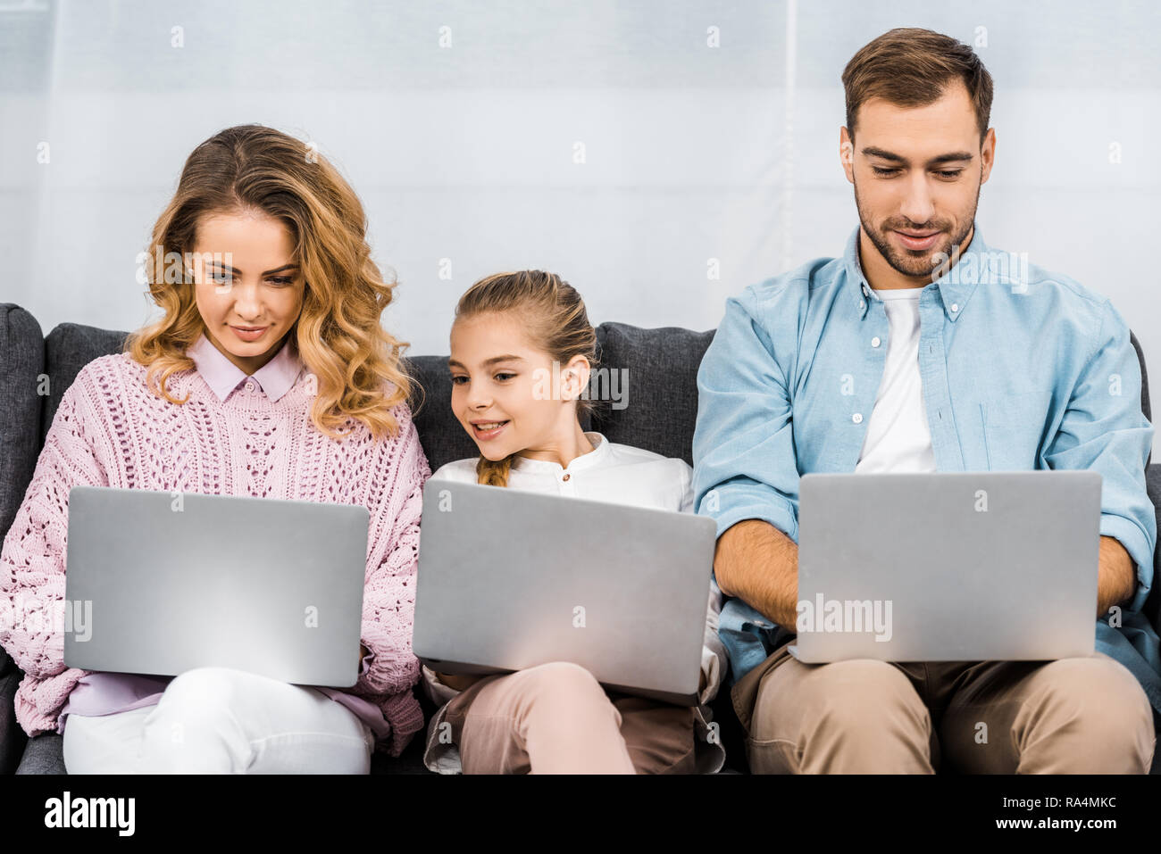 Ragazza carina con due genitori seduti sul divano e utilizzando i notebook in appartamento Foto Stock