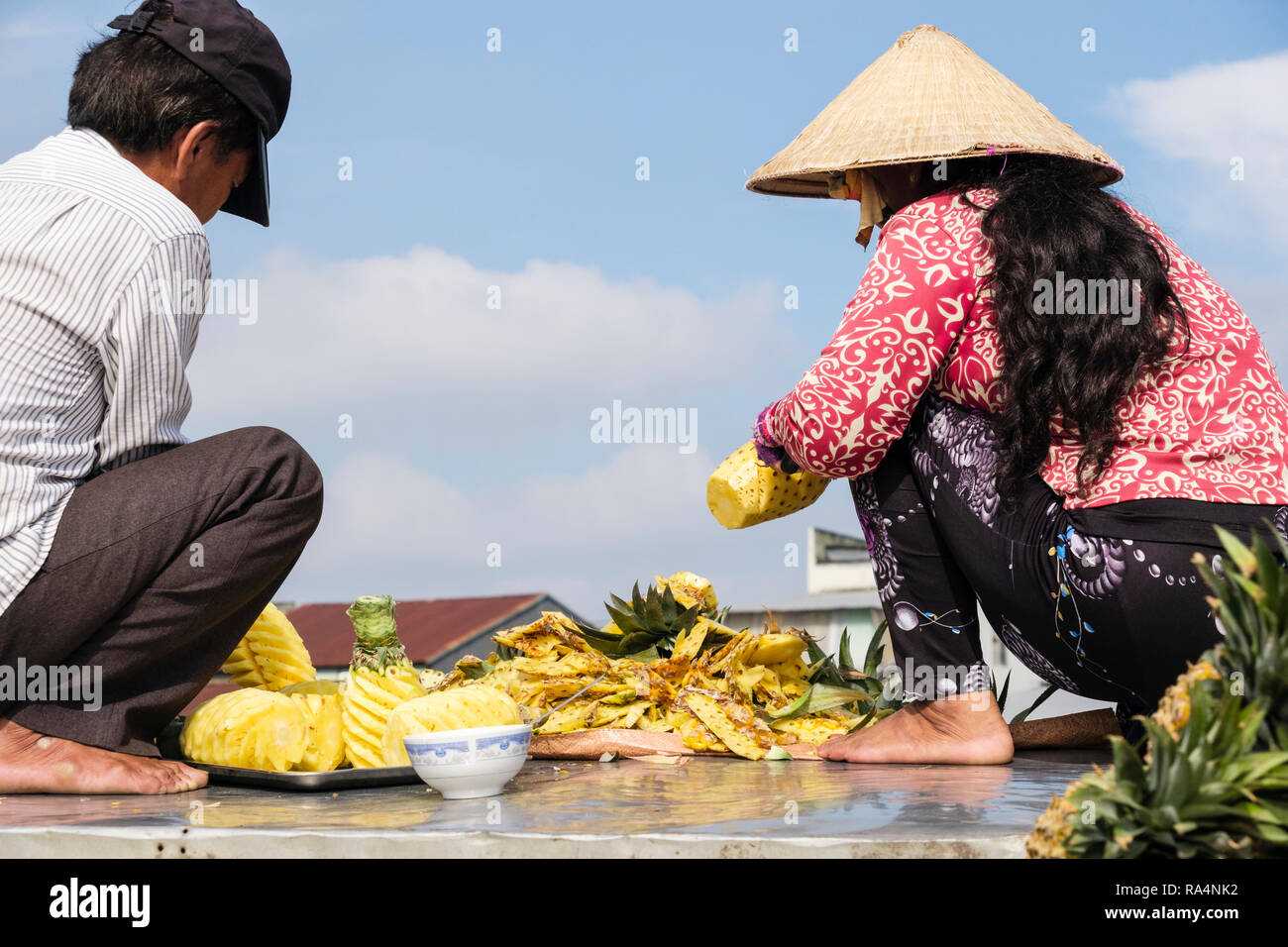 Un vietnamita l uomo e la donna preparare ananas frutta a vendere nel mercato galleggiante sul Fiume Hau. Can Tho, Delta del Mekong, Vietnam Asia Foto Stock