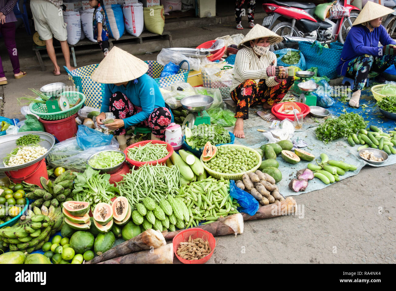 Donne vietnamita stallholders indossando cappelli conici visualizzazione di frutta fresca locale e ortaggi per la vendita in un mercato. Can Tho Mekong Delta Vietnam Asia Foto Stock