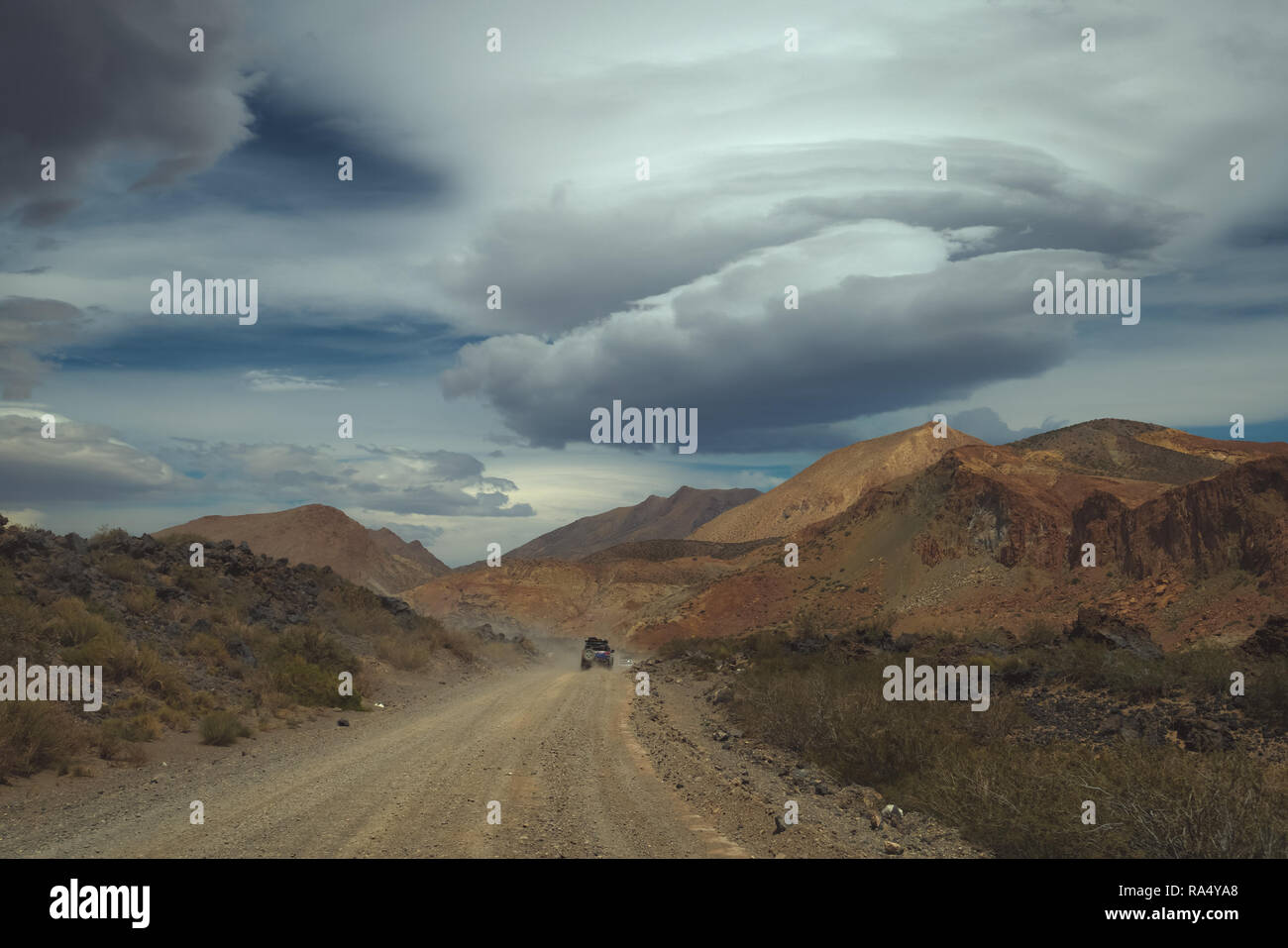 Nuvole lenticolari sulle montagne del Sud America con un veicolo in marcia lungo una strada sterrata in un deserto arido paesaggio Foto Stock