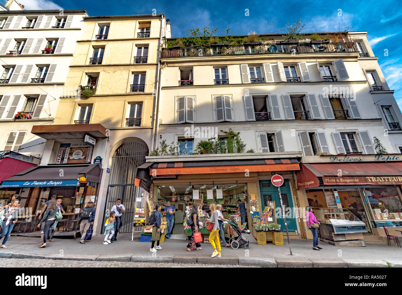 La gente camminare passato negozi ed appartamenti con persiane alle finestre ,nel tardo pomeriggio di sole estivo, Rue Lepic , Montmartre , Parigi Foto Stock
