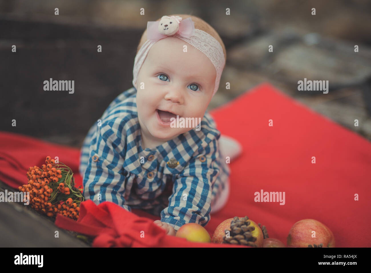 Il bambino neonato ragazza con gli occhi blu che indossa tartan controllare Dress shirt e scialle rosa bandana in posa su legno vecchio stile retrò carro carrello a rotelle con appl Foto Stock