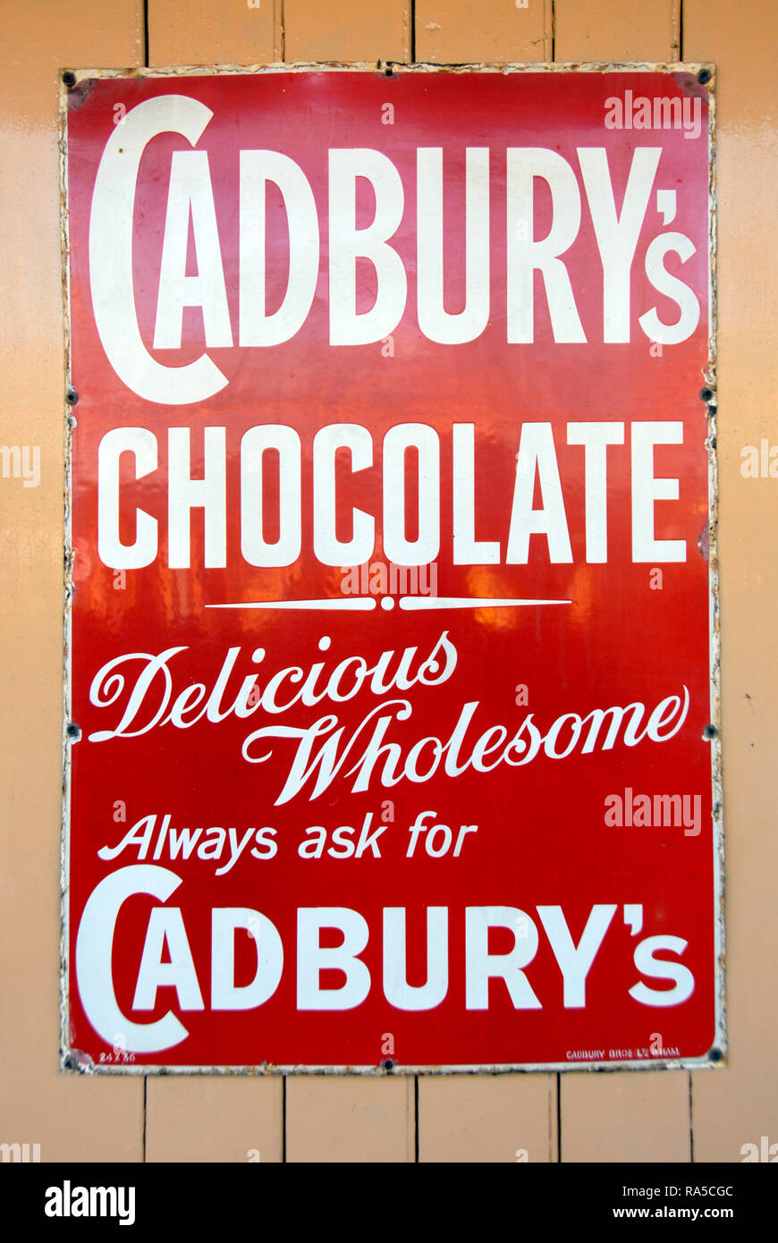 Metallo vecchio pannello pubblicitario per Cadbury's cioccolato, sulla parete alla stazione ferroviaria, Inghilterra Foto Stock