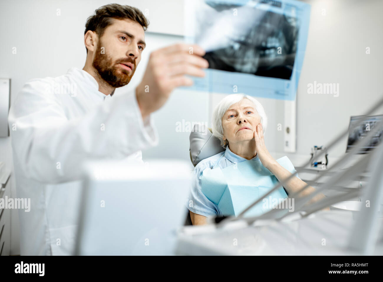 Preoccupato elder donna durante la consultazione con bel dentista che mostra vedute x-ray nello studio dentistico Foto Stock