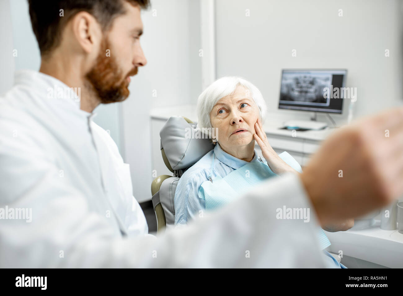 Preoccupato elder donna durante la consultazione con bel dentista che mostra vedute x-ray nello studio dentistico Foto Stock