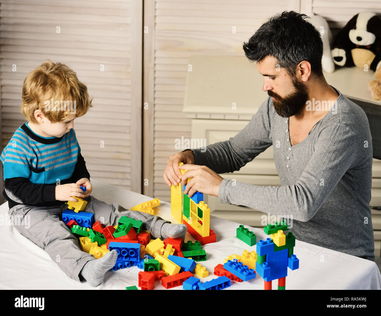 Papà e kid costruire casa di materia plastica in blocchi. Infanzia e giochi  educativi concetto. Uomo e ragazzo giocare su sfondo di legno. Padre e  Figlio con facce occupato creare costruzioni colorate