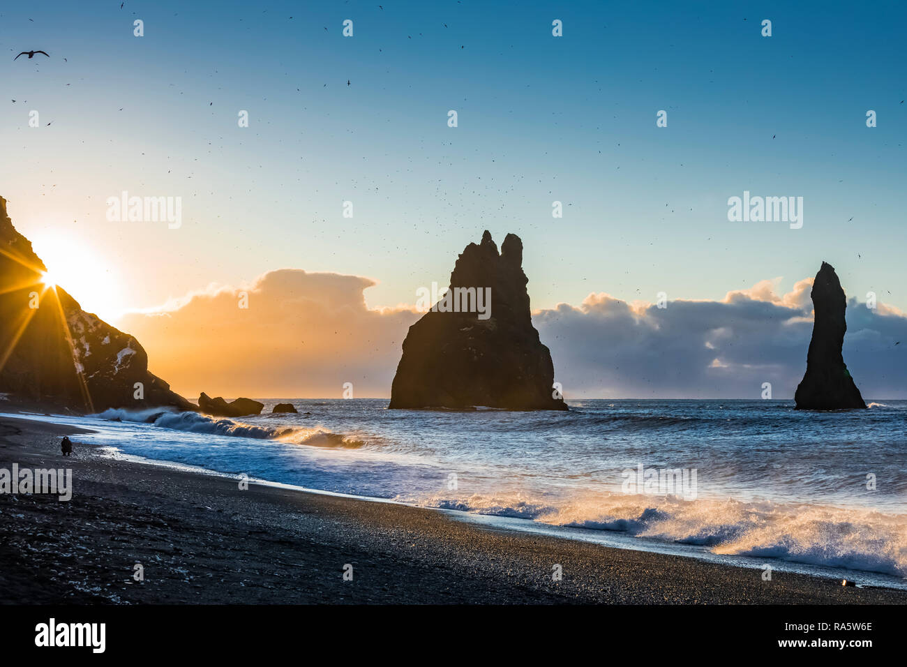 Reynisfjara spiaggia di sabbia nera di prima mattina la luce, con l'Oceano Atlantico onde rotolamento in passato il mare Reynisdrangar pile, noto anche come troll, e Foto Stock