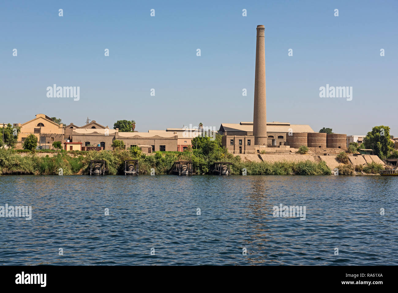 Vista sul grande fiume Nilo in Egitto attraverso il paesaggio rurale con industriali di canna da zucchero di fabbrica con camino Foto Stock