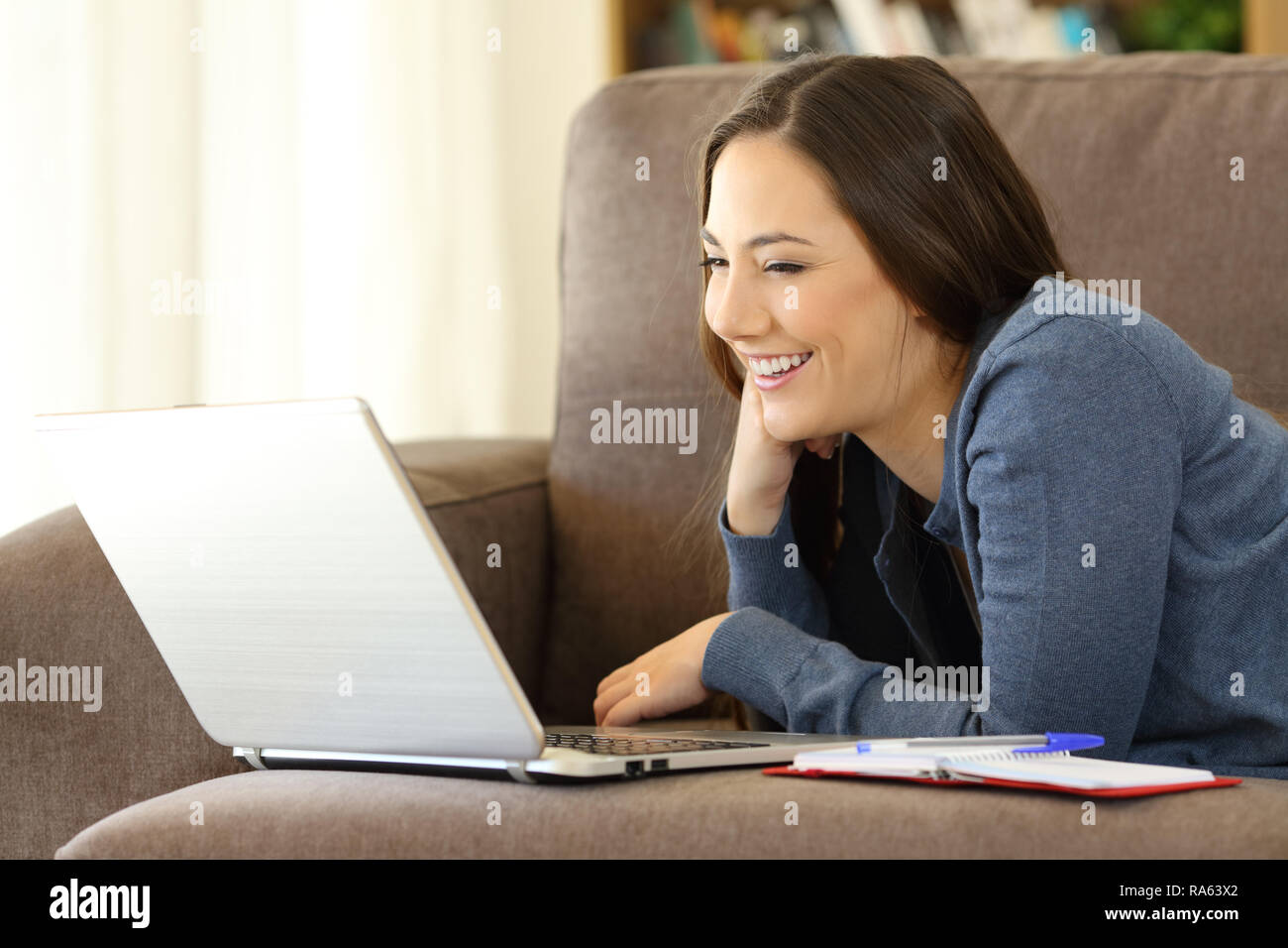 Donna felice la visione di video online su un laptop sdraiato su un lettino a casa Foto Stock