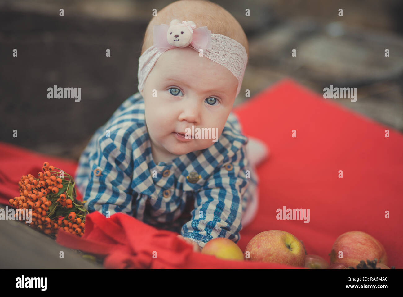 Il bambino neonato ragazza con gli occhi blu che indossa tartan controllare Dress shirt e scialle rosa bandana in posa su legno vecchio stile retrò carro carrello a rotelle con appl Foto Stock