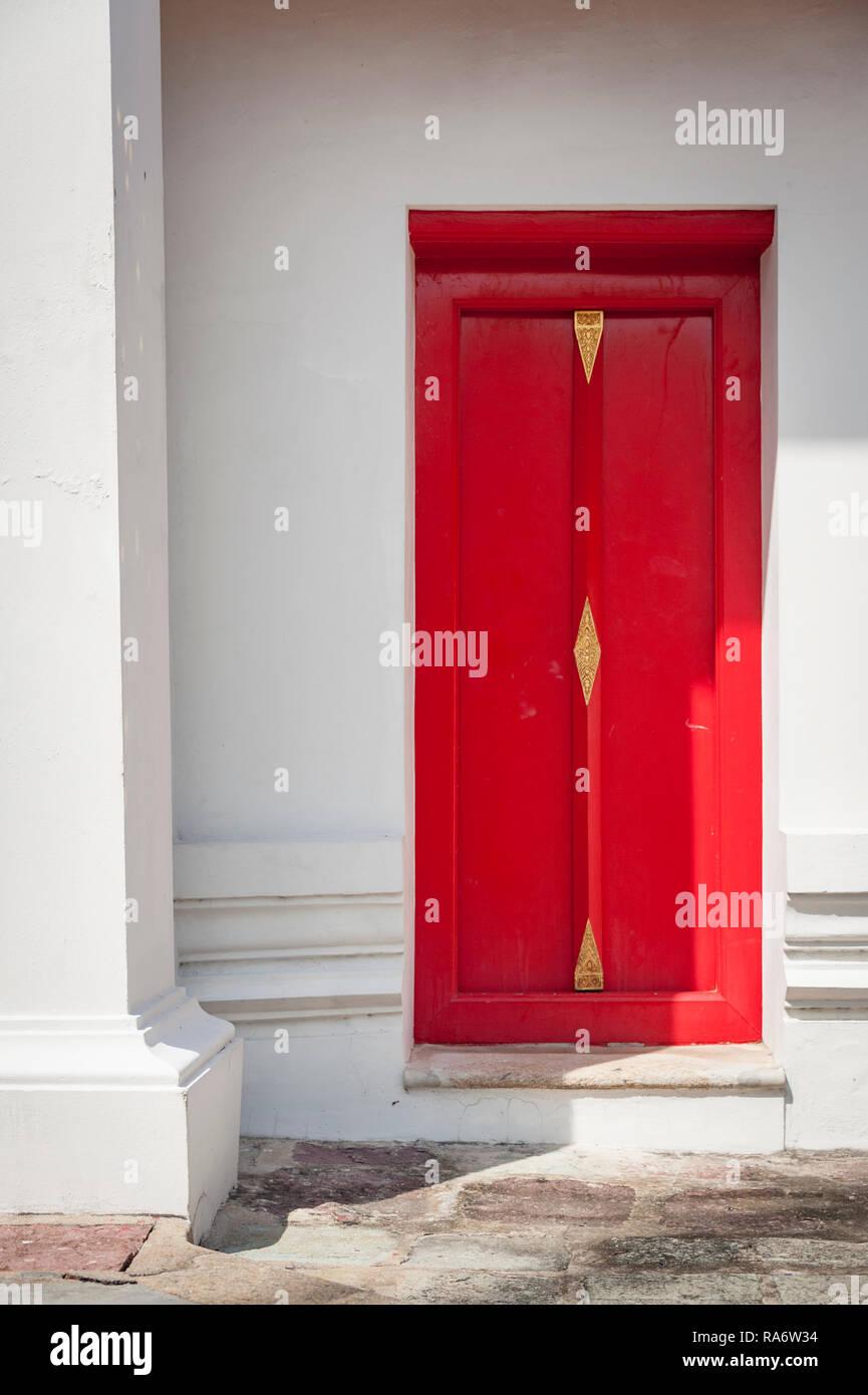 Un rosso brillante porta in una parete bianca tempio thailandese Foto Stock