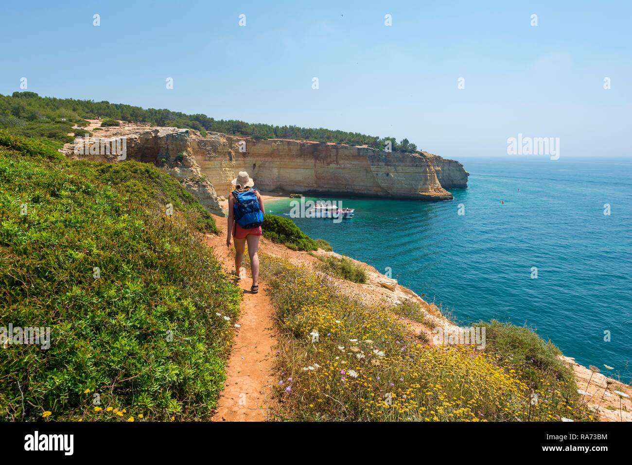 Giovane donna su un sentiero escursionistico, vista sul mare turchese, spiaggia Praia da Marinha, robusto costa rocciosa di arenaria Foto Stock