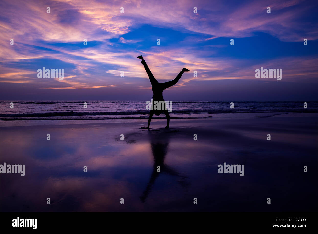 Uomo fa handstand sulla spiaggia al tramonto Foto Stock