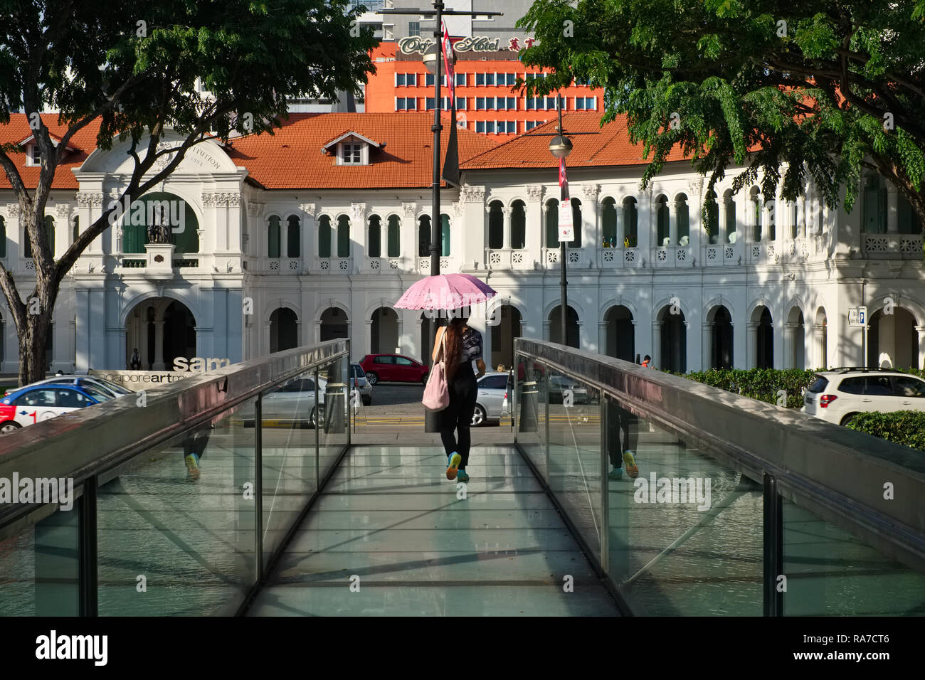 Una giovane donna attraversa un ponte su un laghetto artificiale verso lo stile coloniale, Museo dell'Arte di Singapore (SAM), un ex scuola di missione, Singapore Foto Stock