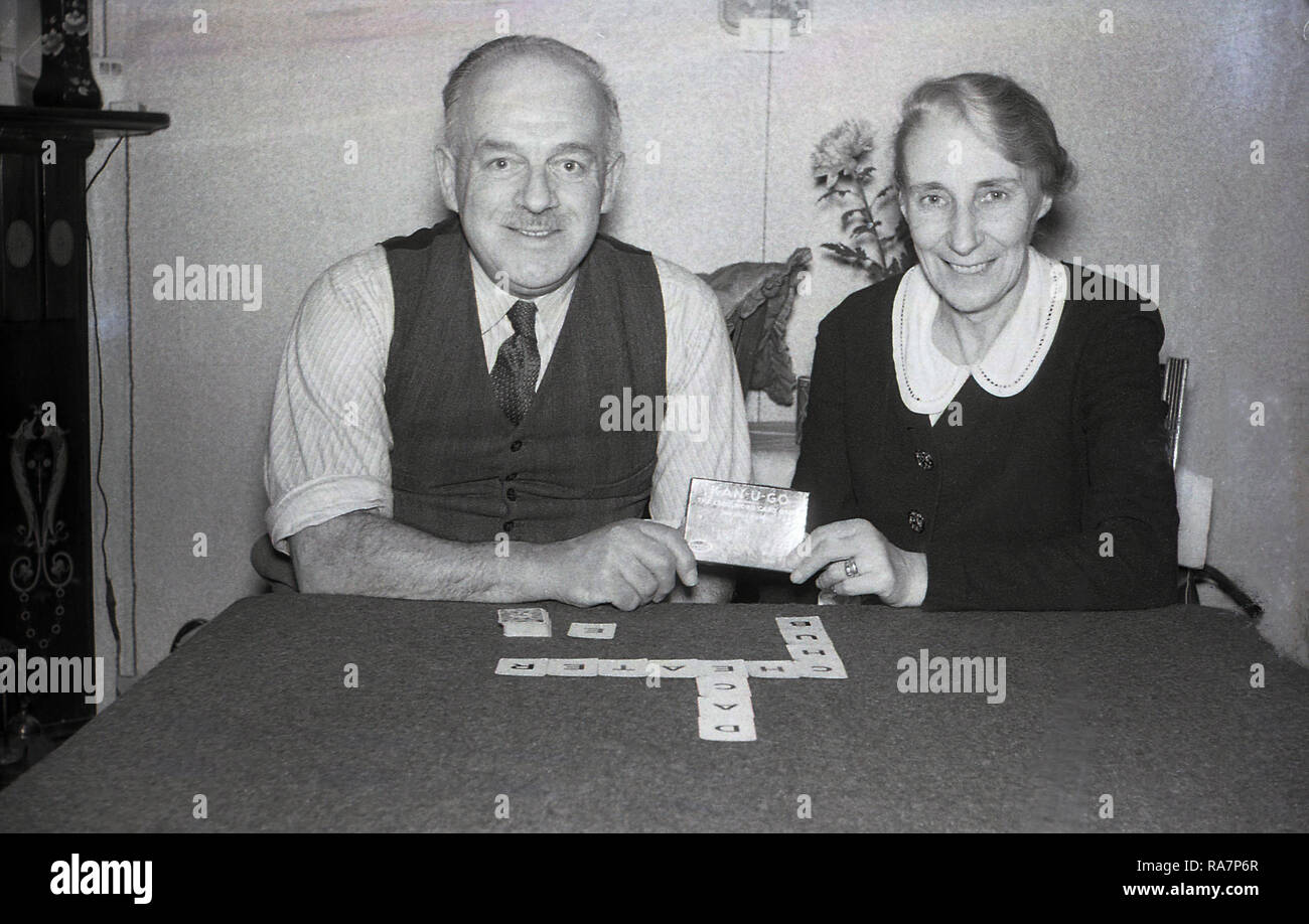 1950, coppia di anziani seduti ad un tavolo da gioco giocare "Kan-U-Go", una vecchia crossword card game, Inghilterra, Regno Unito. Per due a sette giocatori, il gioco proviene dal 1930s e presenta piccole carte con lettere e valori e regole semplici per la riproduzione e la rigatura, Foto Stock