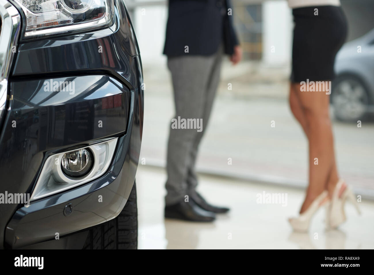 Irriconoscibile donna che indossa in tacchi alti e uomo in piedi nel centro di auto. Close up di costosi nero auto faro. Manager della concessionaria auto con clienti di sesso femminile. Foto Stock