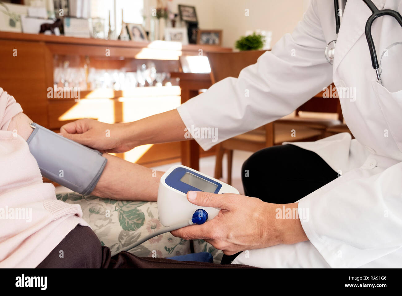 Primo piano di un medico caucasica uomo in camice bianco, la misurazione della pressione del sangue di un senior caucasian paziente donna con uno sfigmomanometro, al suo h Foto Stock