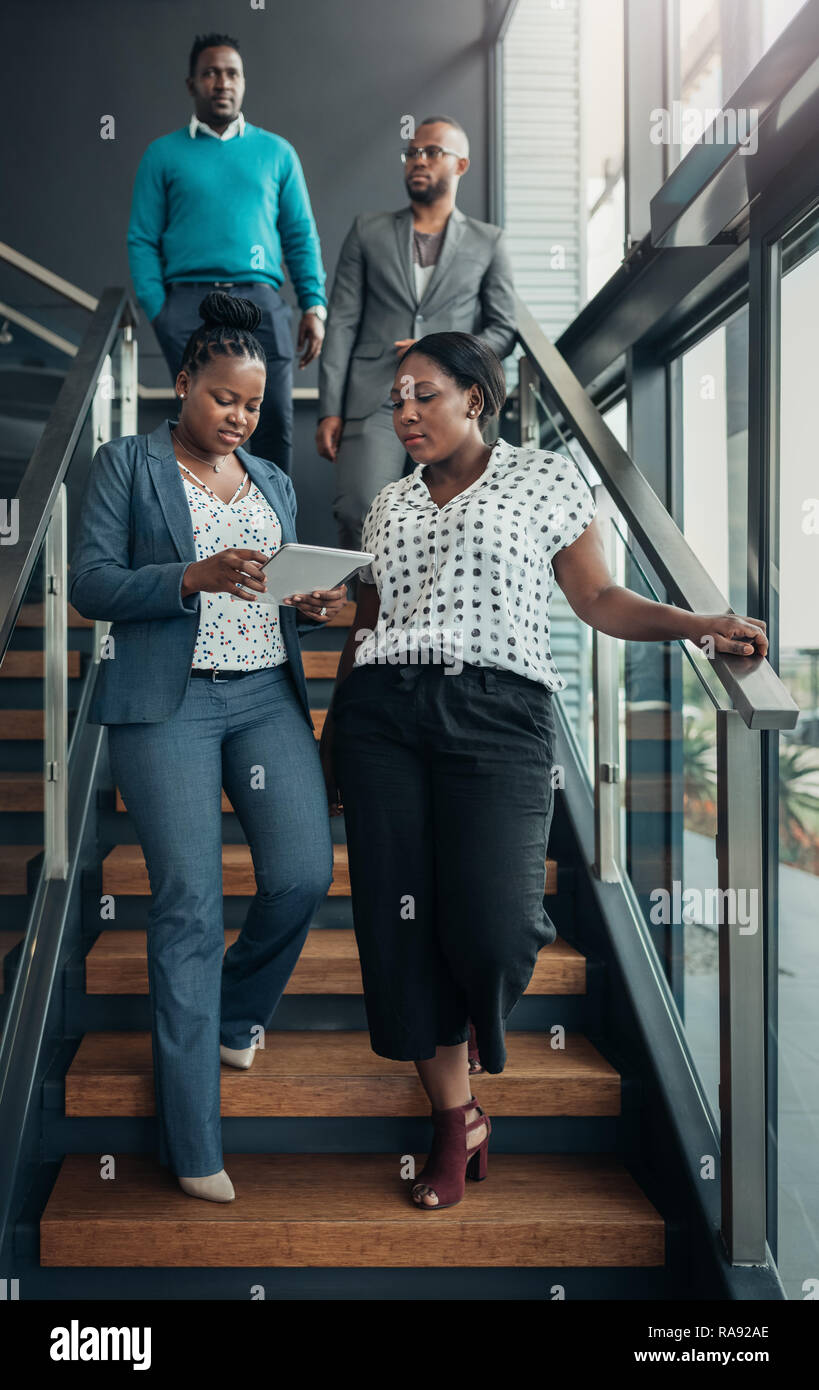Il Team di business in Africa la gente camminare giù per una scalinata dopo una riunione il signore davanti sono a parlare mentre si utilizza un tablet Foto Stock