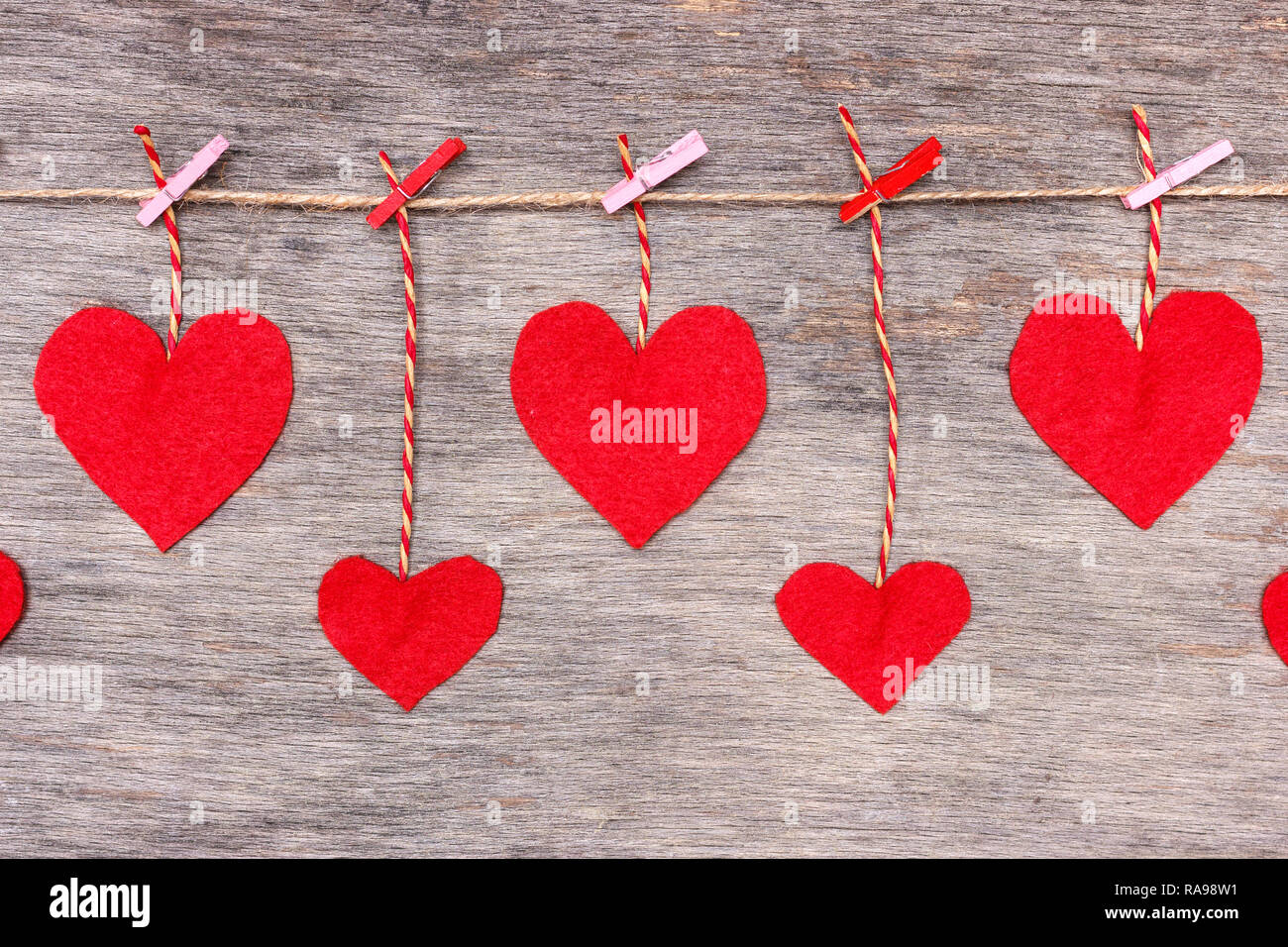 Rosso di San Valentino di cuori sul cordoncino naturale e spine di rosa appeso sul rustico sfondo texture, spazio di copia Foto Stock