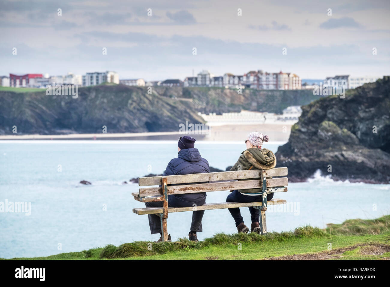 La gente seduta su una panchina lungo la costa che si affaccia sul mare a Newquay in Cornovaglia. Foto Stock