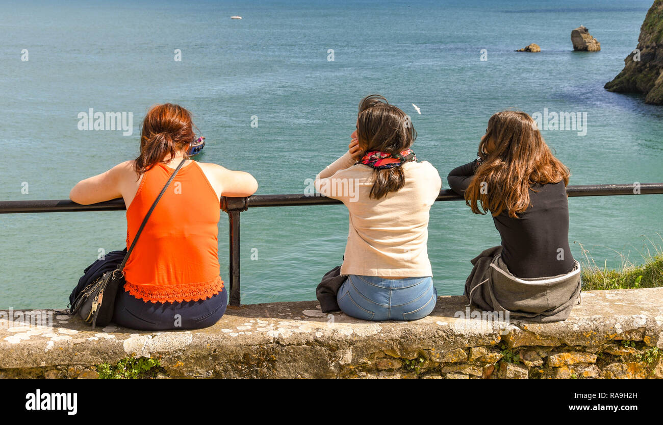 TENBY, Pembrokeshire, Galles - Agosto 2018: tre giovani seduti su una parete sulla via costiera che guarda al mare in Tenby, West Wales. Foto Stock