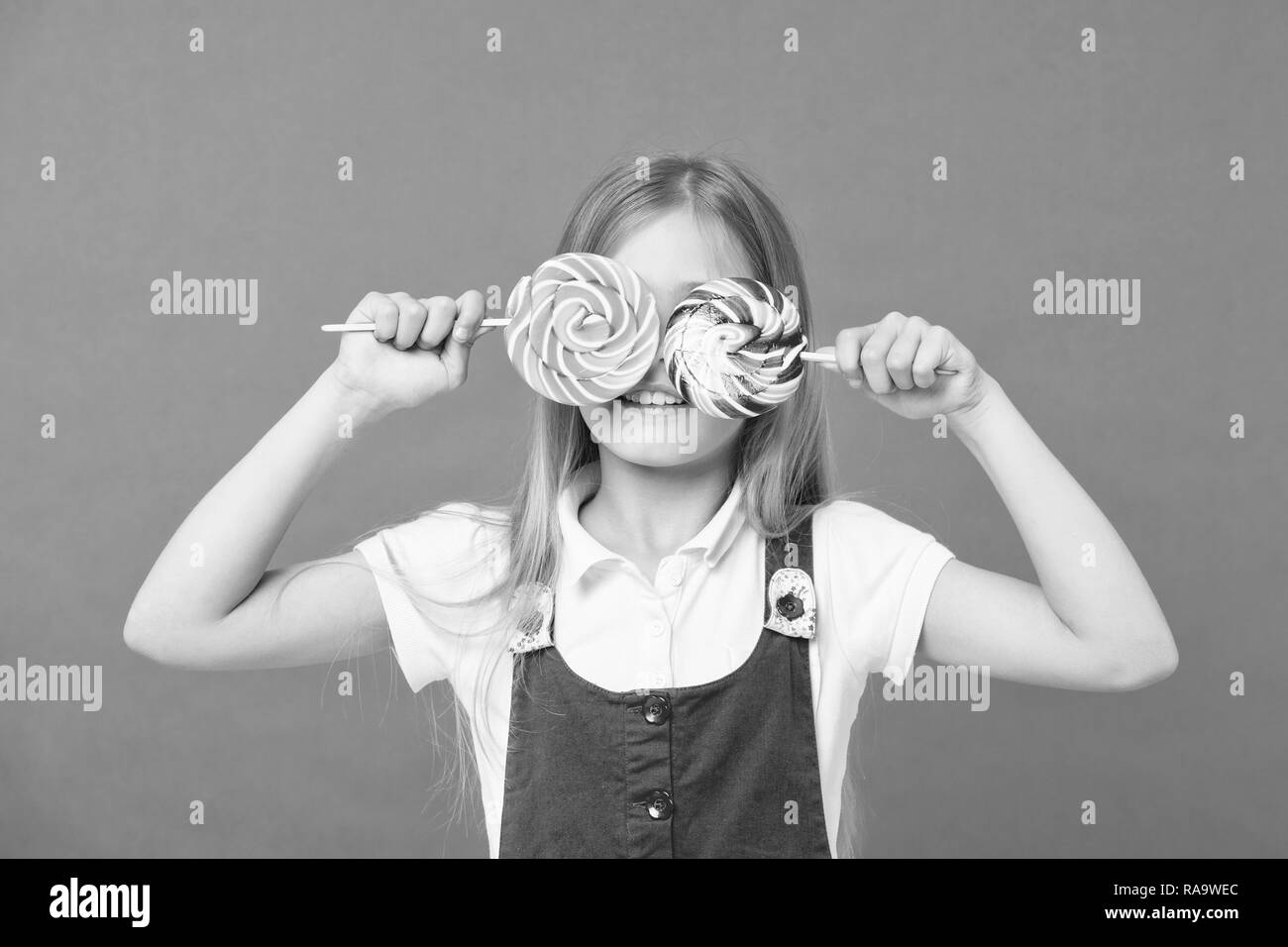 Funny bambino con connettori lollipop su sfondo viola. Capretto piccolo sorriso con caramelle su bastoni su sfondo viola. Ragazza sorridente con caramelle di turbolenza. Cibo e dessert. La bellezza con la caramella. La dieta e dieta. Foto Stock