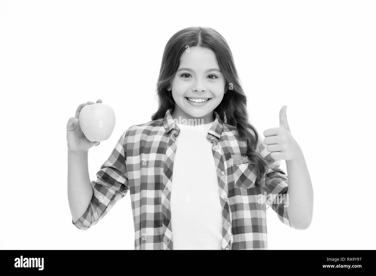 Ragazza carina lunghi capelli ricci contiene frutta apple sfondo bianco. Bambino ragazza abiti casual detiene apple e mostra il pollice verso l'alto. Bambino kid faccia felice gradisce frutti. Scuola di concetto di snack. Alimentazione sana Dieta. Foto Stock