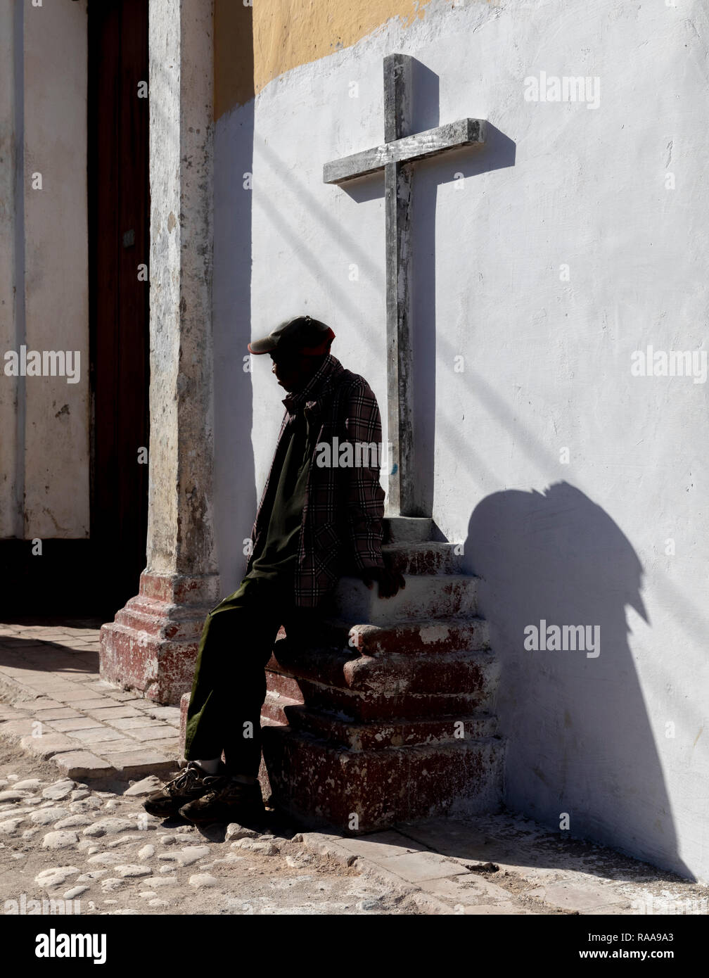 Uomo seduto sul piedistallo della croce, Calle Amargura, Trinidad, Cuba Foto Stock