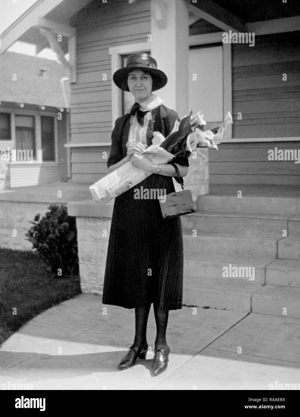 Una donna sta con un mazzo di fiori di fronte alla sua casa di Colorado, ca. 1928. Foto Stock