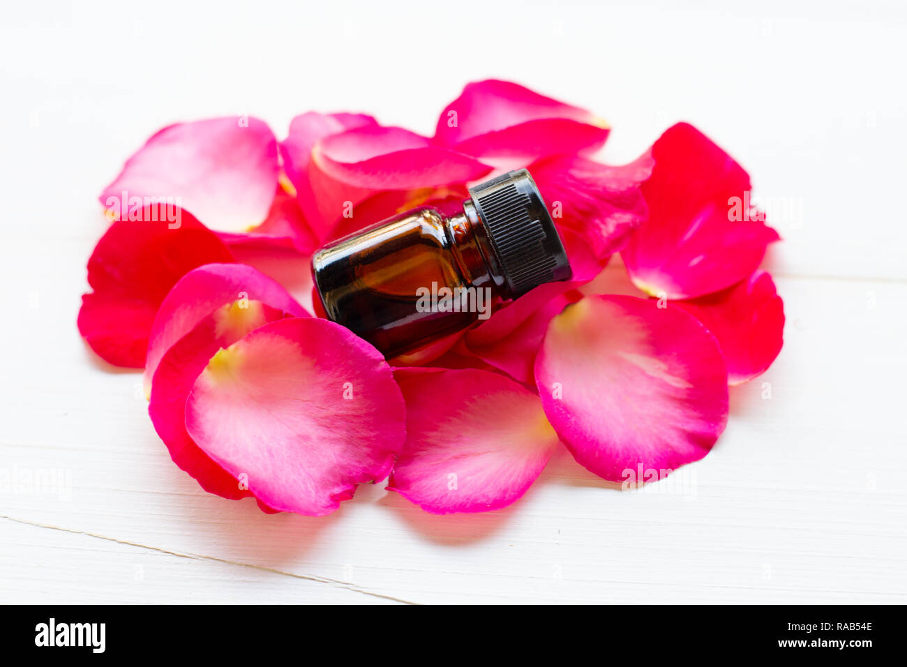 Olio essenziale di petali di rosa sul bianco sullo sfondo di legno. Foto Stock