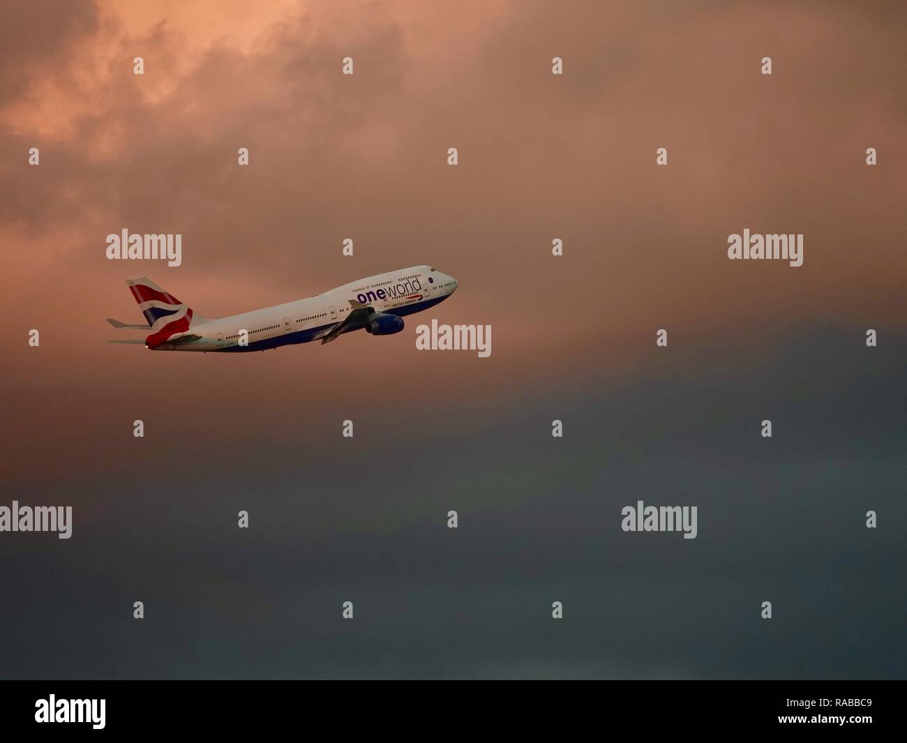 British Airways jumbo jet con One World logo, insieme contro le nubi colorata di rosa e grigio impostando sun, il decollo dall'Aeroporto Internazionale di Miami. Foto Stock
