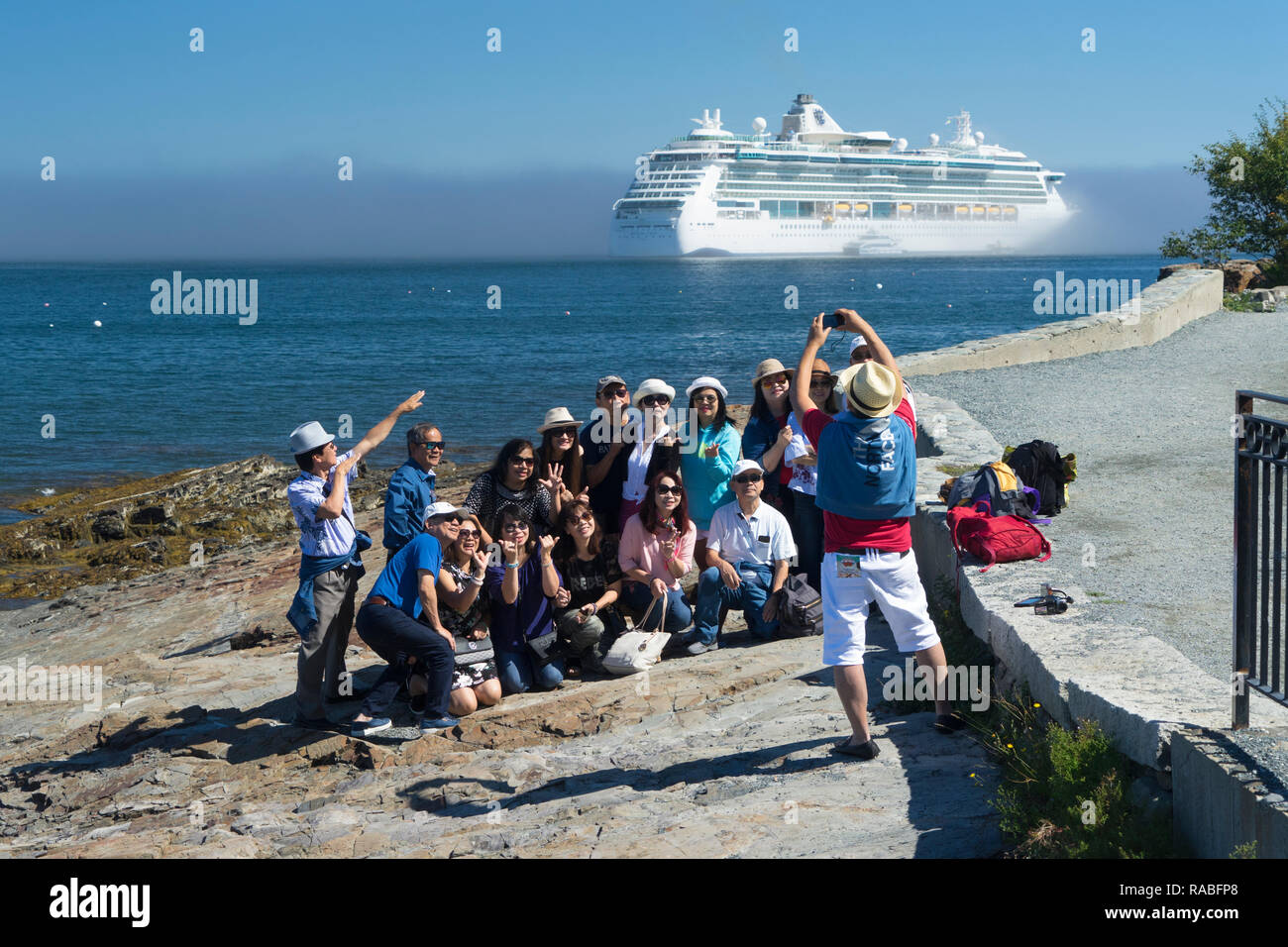 Turisti asiatici di prendere una foto di gruppo con una nave da crociera in background, Bar Harbor, Maine, Stati Uniti d'America. Foto Stock
