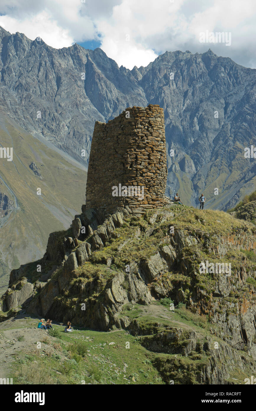 I turisti del trekking da una torre vicino al Gergeti chiesa della Santa Trinità dal fiume Chkheri, sotto il monte Kazbegi nel Caucaso, Georgia Foto Stock