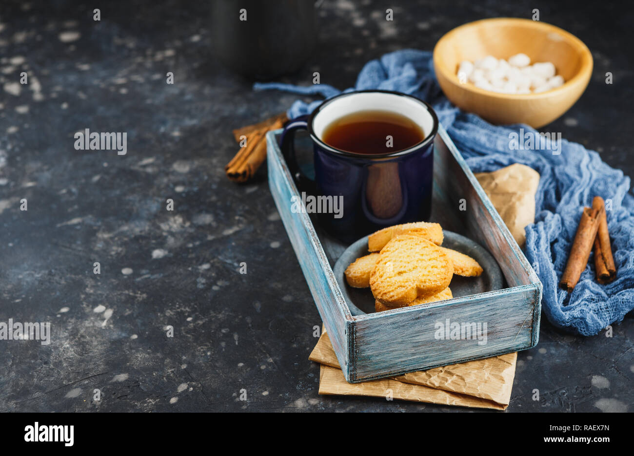 Smaltato blu tazza di tè, bastoncini di cannella, anice stelle e pasta frolla su uno sfondo scuro. Spazio per il testo. Foto Stock