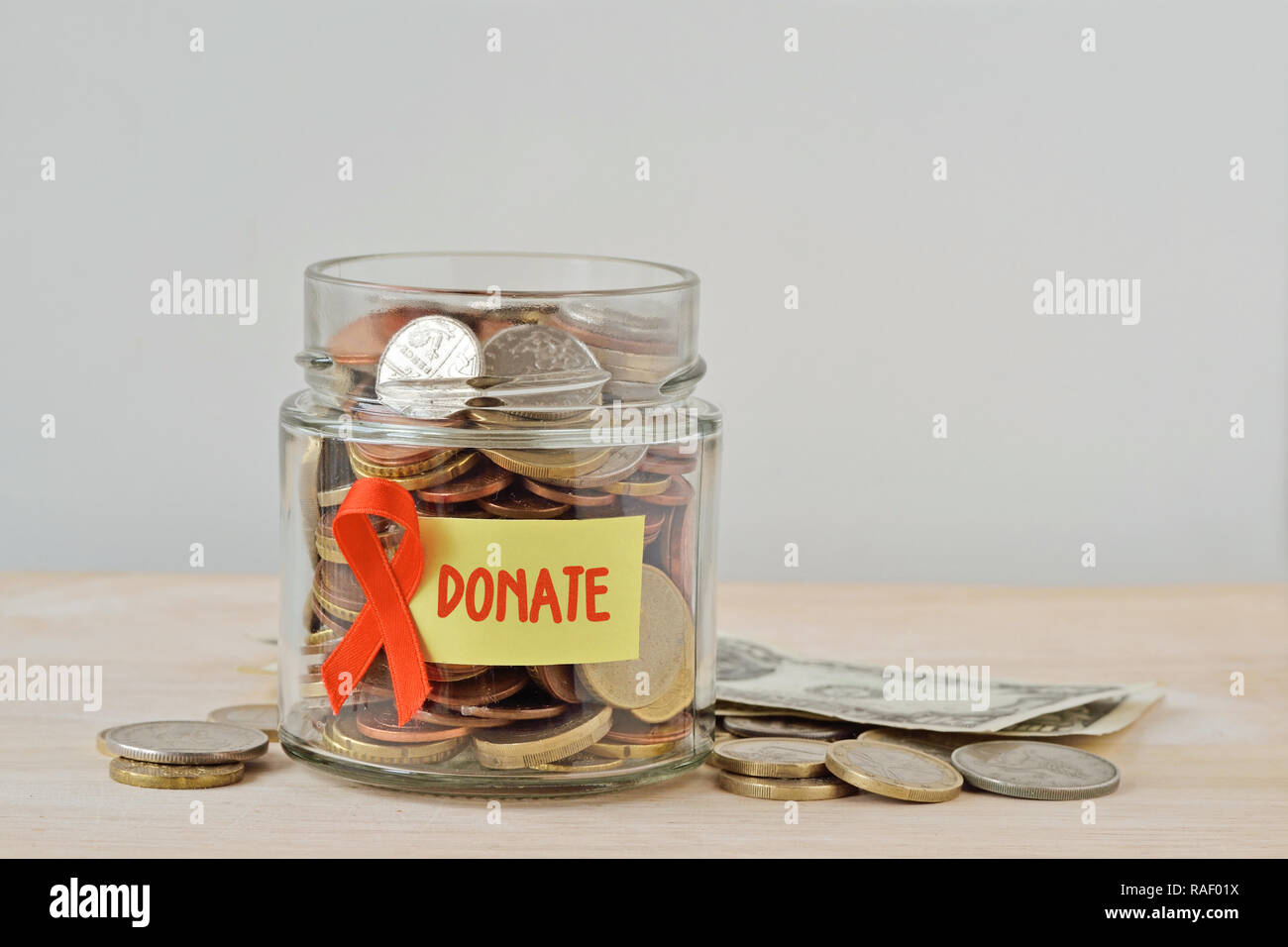 Soldi jar piena di monete con il nastro arancione e donare etichetta - Concetto di leucemia, cancro del rene, la sclerosi multipla e l'abuso di animali della carità Foto Stock
