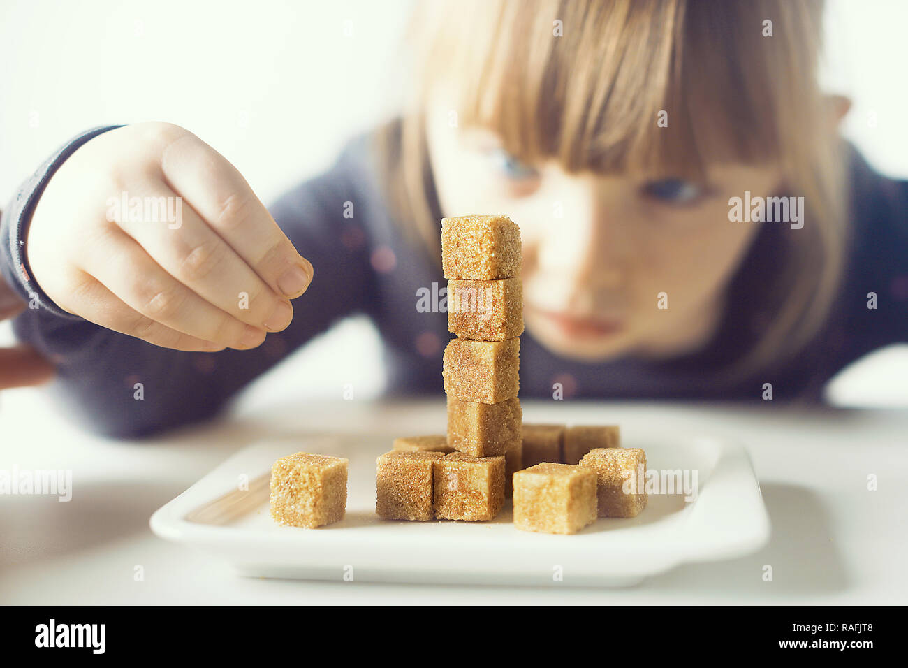 Bambino, cubetti di zucchero. Il problema del consumo eccessivo di zucchero da parte di bambini di età inferiore ai dieci anni. Foto Stock