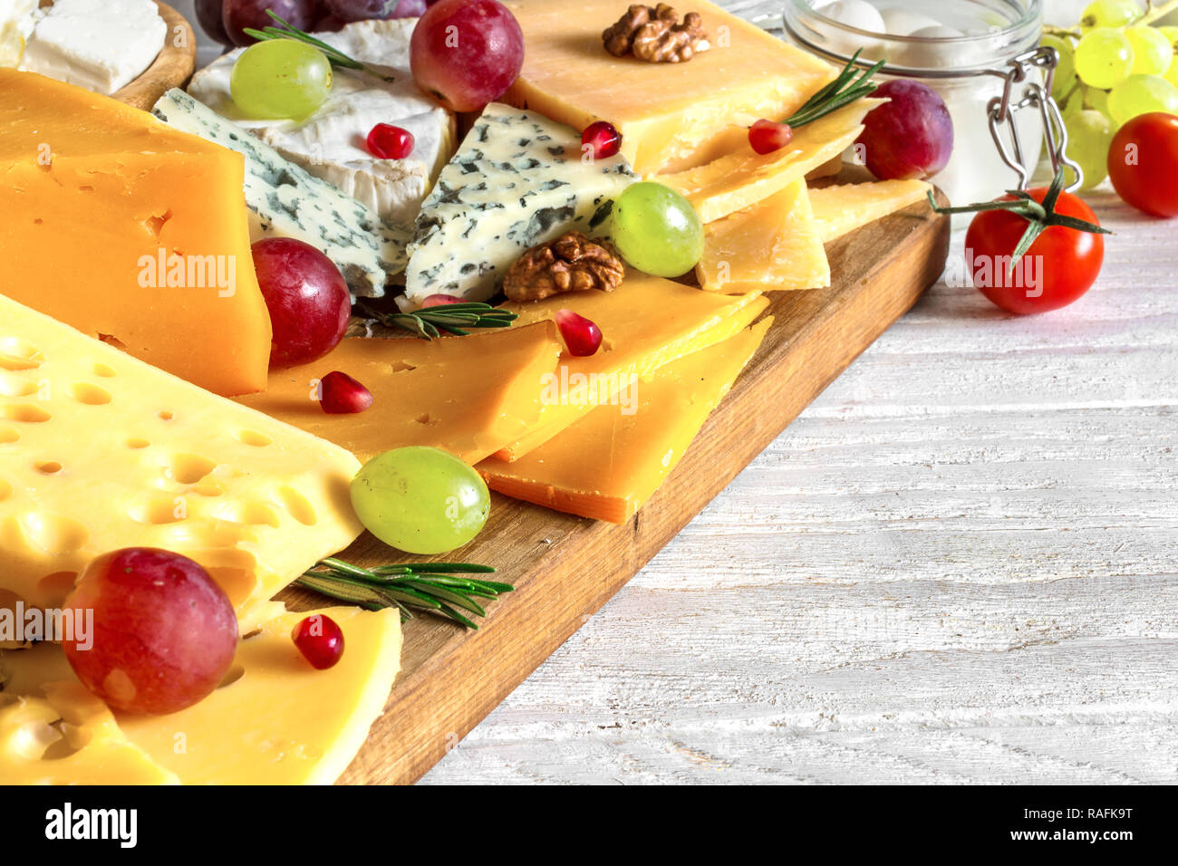 Vari tipi di formaggio con uve, rosmarino, pomodori e melograno sul tagliere di legno. close up Foto Stock