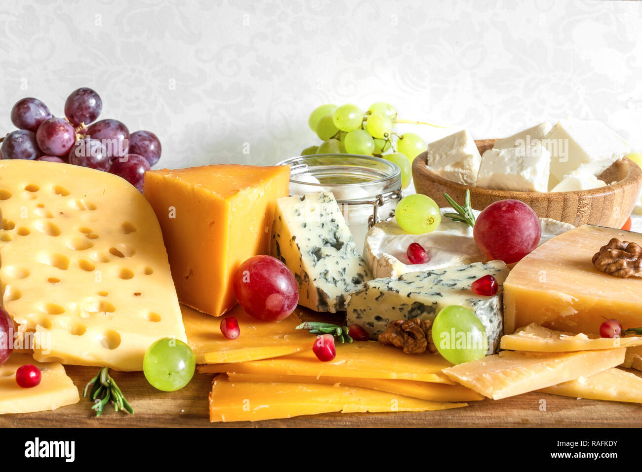 Vari tipi di formaggio con uve, rosmarino e melograno sul tagliere di legno. close up Foto Stock