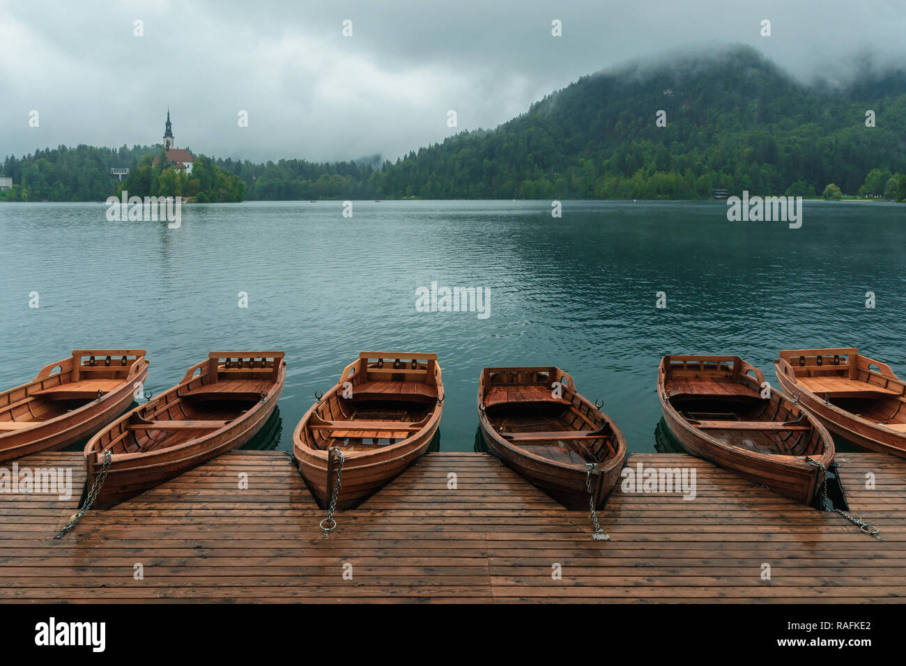 Bled con il lago, isola, castello, barche e le montagne sullo sfondo di Misty e giornata piovosa, Slovenia, Europa Foto Stock